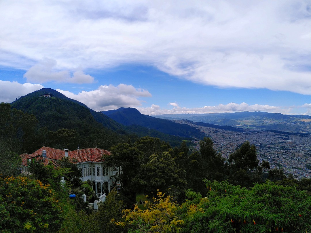 A villa between trees on a green mountain, fading into a huge city to the right