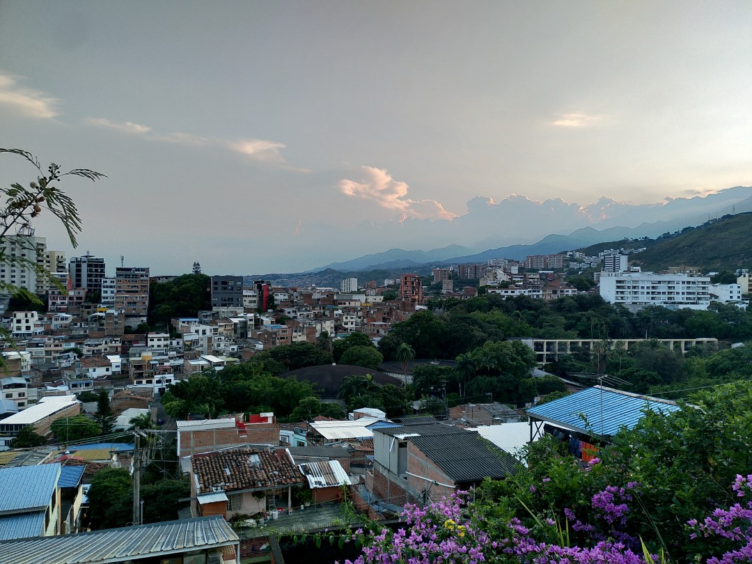 View of a cities roofs on the left and tree-covered mountains merging under the evening sky in the middle