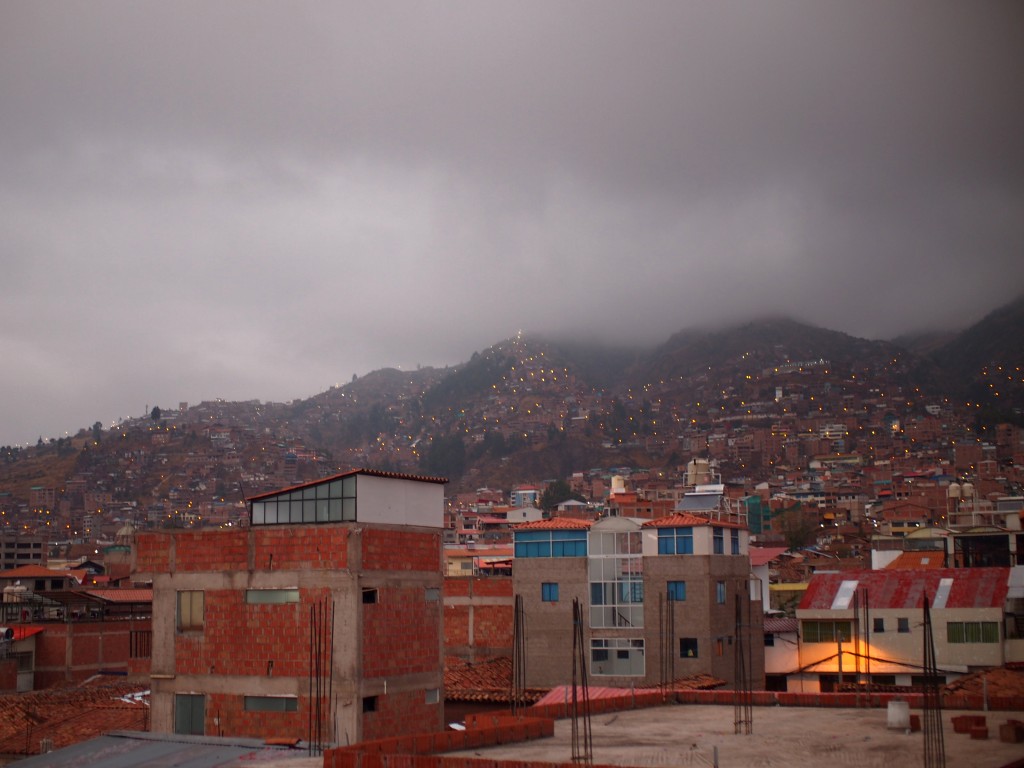 View up a hill reaching into the clouds, full of Peruvian buildings with street lights visible between them