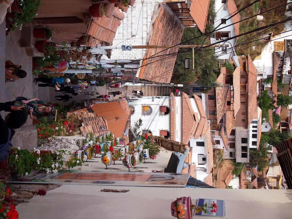 A narrow alley with stairs between white buildings with terracotta roofs and pottet plants at their walls