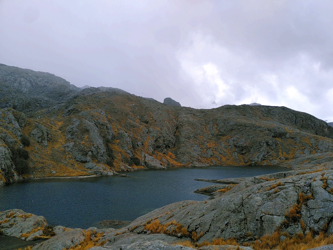 A blue-grey mountain lagoon surrounded by dark grey rock and foggy clouds