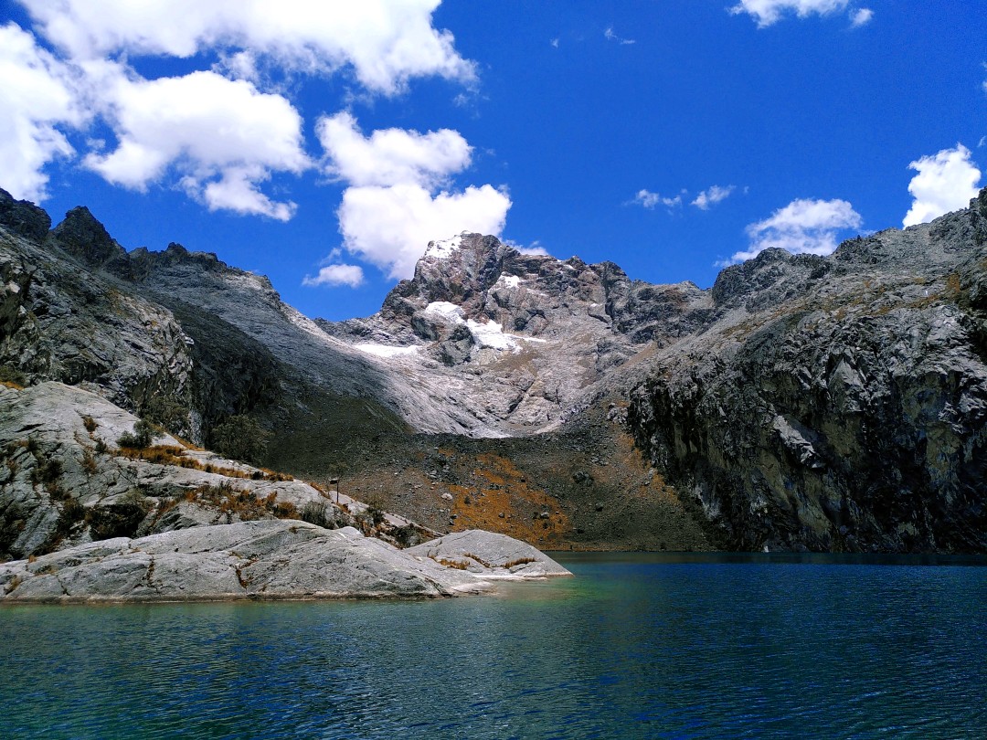 A blue mountain lagoon in front of grey rocky mountains and blue sky