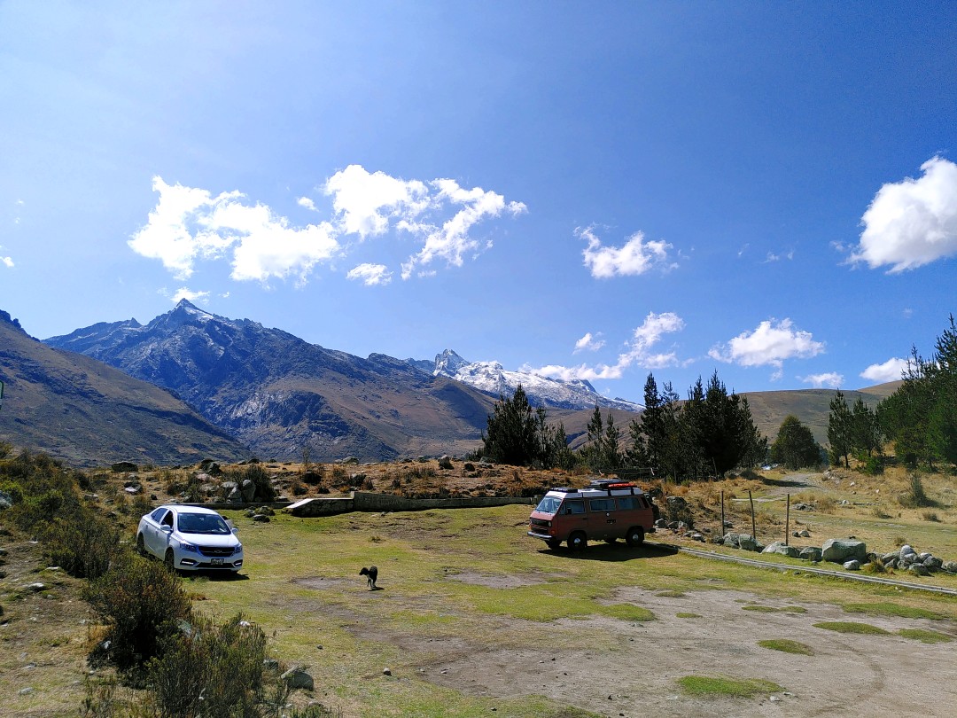 A white car and an orange van parked on a field with view on snow-capped Andean mountains