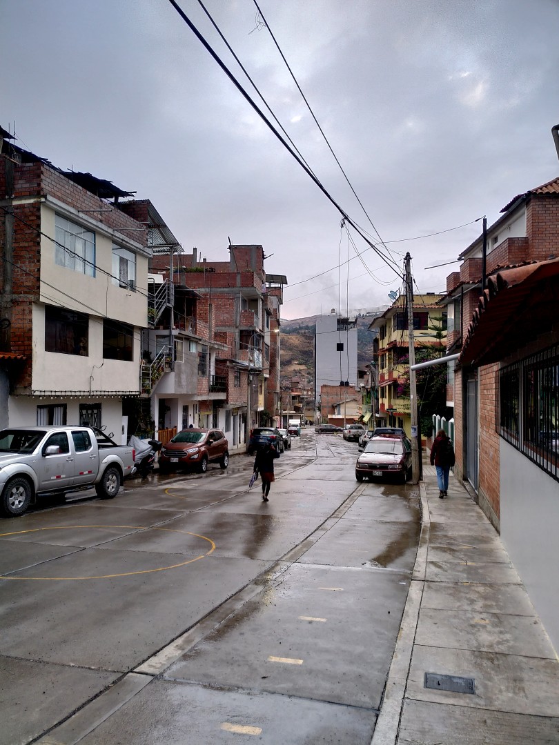 Buildings, cars and some people in a wet street with cables overhead