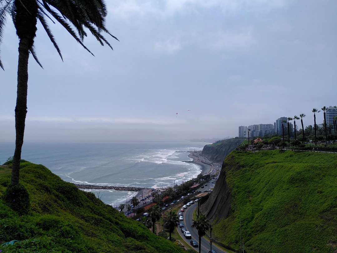 View along Lima's coast, with the ocean on the left and a road under cliffs to the right