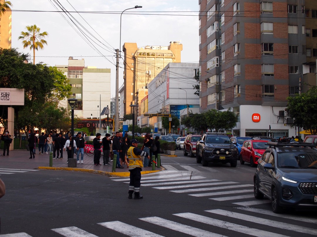 A busy crossing between multi-story building with a police man controlling the car traffic