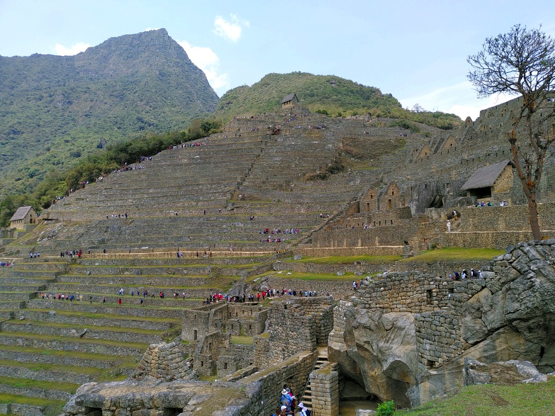 Stone walls of former Inka buildings on the side of a mountain with people walking between them