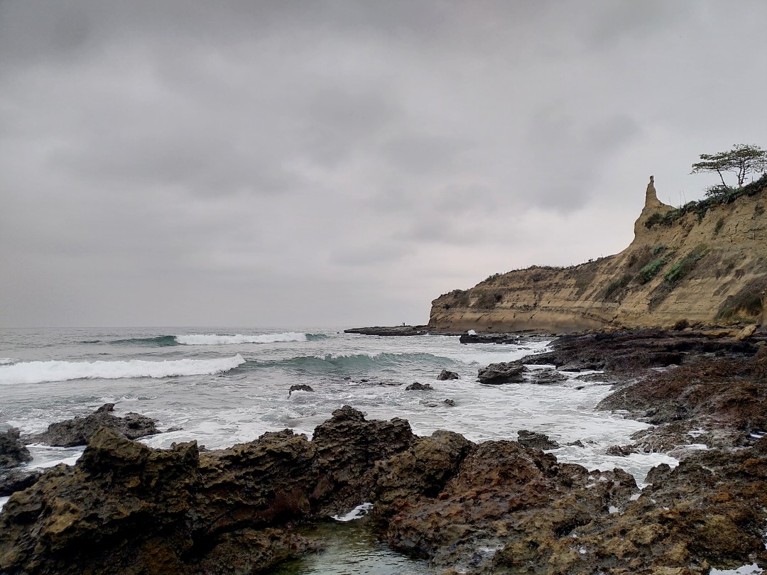 Rocks in front of waves on the ocean under a grey sky