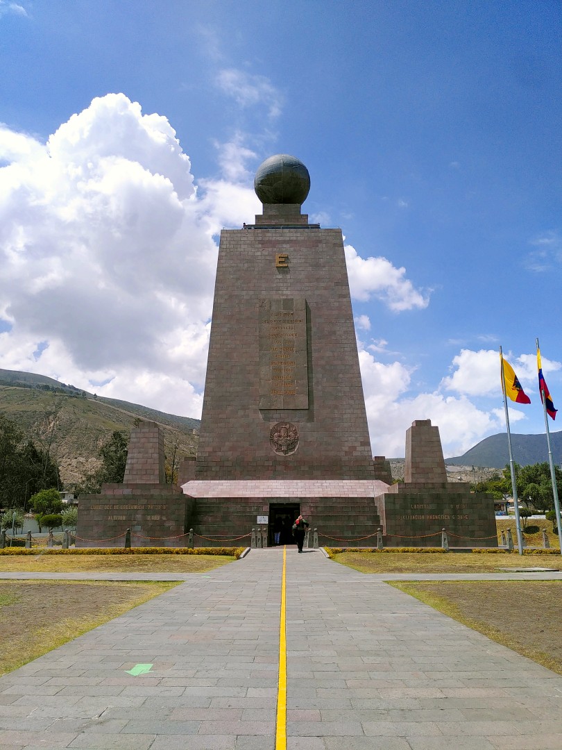 A yellow line on a stone walkway leading up to a massive looking stone tower with steel globe on its top