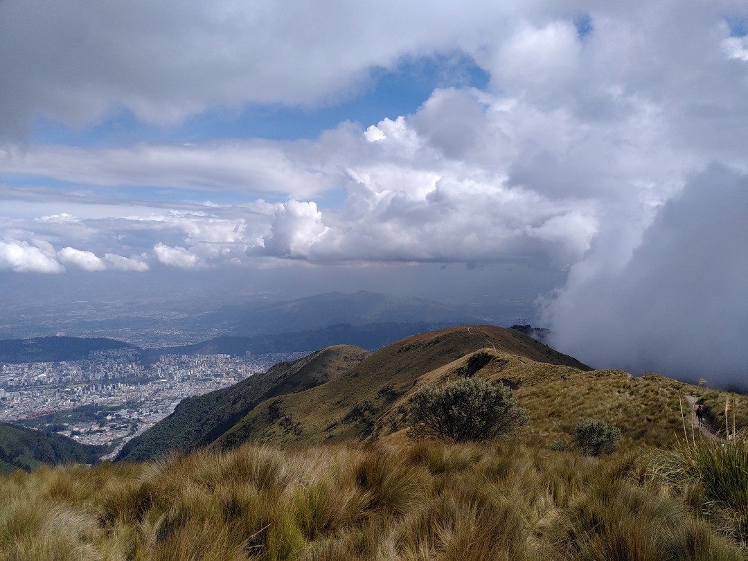 Panorama of the city of Quito behind some Andean grass from a mountain, spectacularly framed by mixed sun and clouds