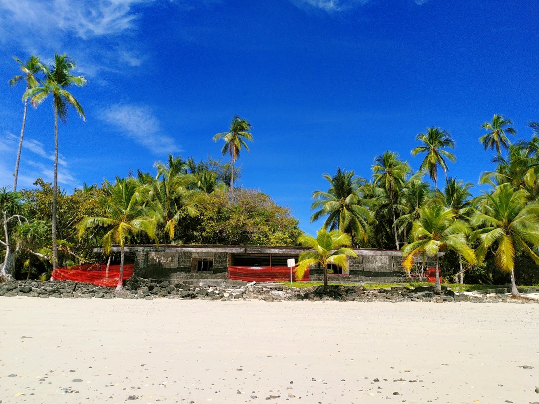 An abandoned flat building sitting in front of the forest on the beach