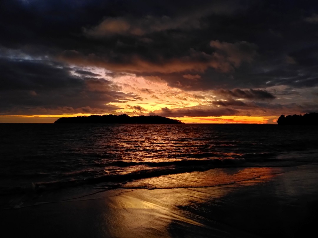 Panorama of a dark sea and schemes of an island with some orange lightning left shortly after sunset